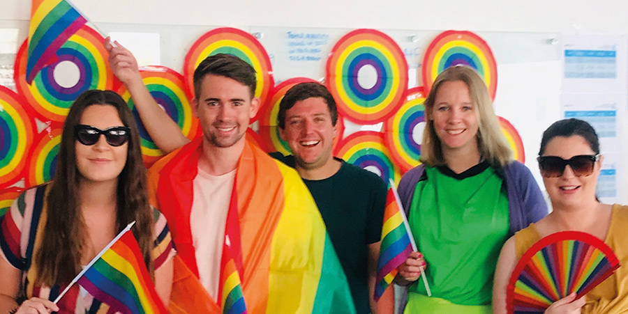Group of young people dressed to Pride parade, wearing rainbow clothes and smiling.