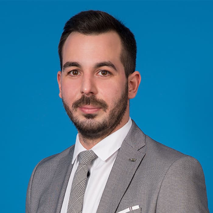 Young man with beard looking into the camera in front of blue background.