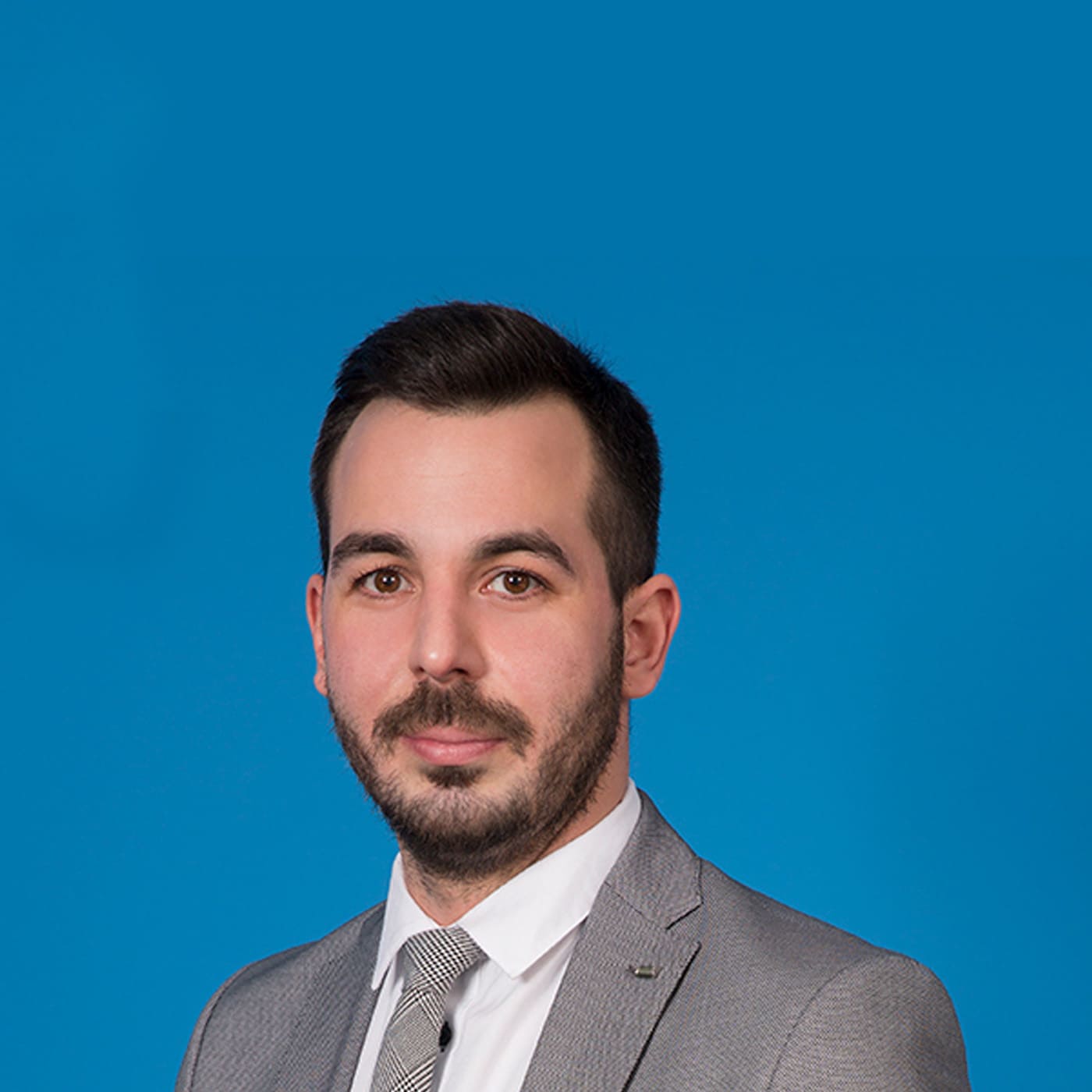 Young man with beard looking into the camera in front of blue background.