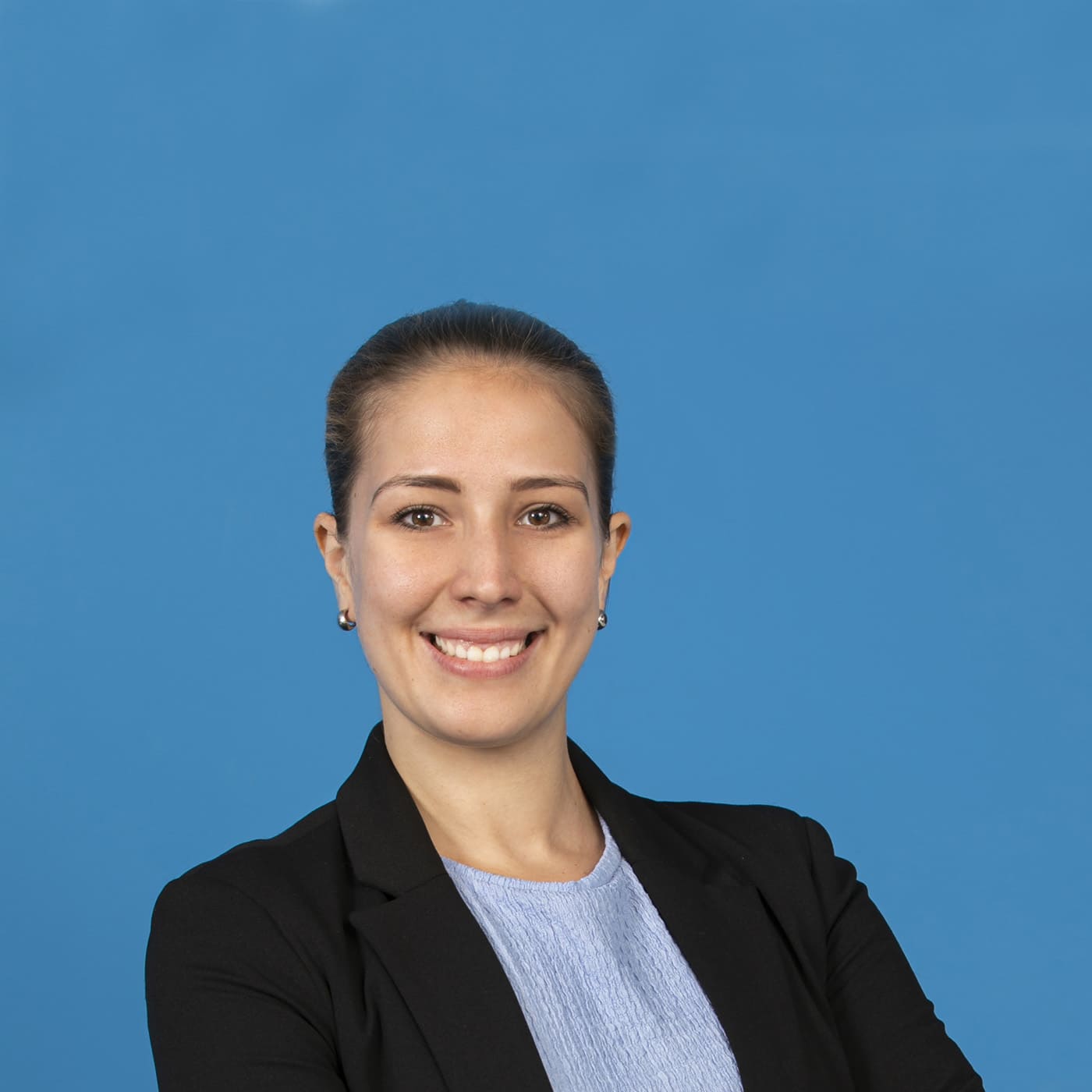 Young blonde woman smiling into the camera in front of blue background.