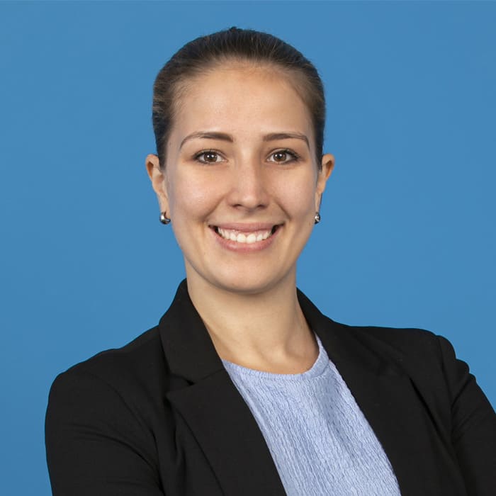 Young blonde woman smiling into the camera in front of blue background.